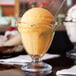 A glass cup with a Anchor Hocking Crystal Footed Sherbet Dish filled with orange ice cream and a spoon.