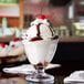 A close-up of an Anchor Hocking Crystal Footed Sherbet Dish filled with ice cream topped with chocolate and a cherry.
