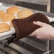 A hand using a San Jamar terry cloth pot holder to hold a tray of bread.