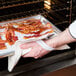 A person using a San Jamar Bestex terry cloth pad to hold a tray of bacon.