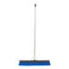 A blue Carlisle commercial push broom with a black handle.