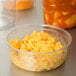 A Fabri-Kal clear plastic deli container of macaroni and cheese on a counter next to a bowl of soup.