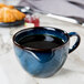 A Tuxton TuxTrendz Artisan Night Sky blue china cup filled with a beverage on a table.