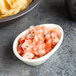 An eggshell Tuxton teardrop ramekin filled with salsa next to a bowl of chips on a table.