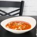 A Tuxton oval china bowl filled with soup with noodles and vegetables.