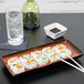 A Tuxton china tray with sushi rolls and chopsticks on it.