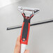 A hand holding a Unger ErgoTec window squeegee with a red and black handle.