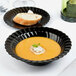 A Fineline Flairware black plastic bowl filled with soup and a piece of bread on a table.