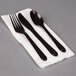 A white napkin with a black fork and spoon wrapped in black plastic.