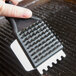 A hand using a Waring grill brush to clean a panini grill.