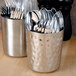 A close-up of a hammered stainless steel French fry cup filled with silverware.