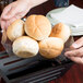A person holding a tray of bread rolls with an American Metalcraft PET basket liner inside.