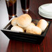 A black American Metalcraft PET basket liner with rolls of bread in it.