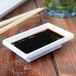 A white rectangular Thunder Group sauce dish with a small amount of sauce on a table with soy sauce and chopsticks.