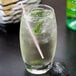 An Arcoroc Salto cooler glass of liquid with ice and a straw and mint.