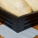A rectangular black American Metalcraft bread basket with bread inside on a table.
