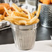 A silver mini stainless steel round trash can filled with french fries on a table.
