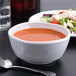 A white melamine bowl filled with soup next to a bowl of salad with a spoon.