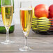 Two Arcoroc champagne flutes filled with champagne next to a basket of apples on a table.