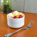 An Arcoroc Rondo white bowl filled with fruit with a fork next to it.