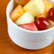 An Arcoroc white china bowl filled with fruit on a table.
