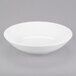 An Arcoroc white coupe bowl on a gray surface.