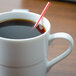 A white Arcoroc coffee mug filled with coffee and a red straw with a straw in the coffee.