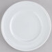 An Arcoroc white porcelain bread and butter plate with a circular edge on a gray surface.