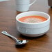 An Arcoroc Rondo cereal bowl of soup with a spoon on a table.