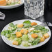 A close-up of a 10 Strawberry Street white porcelain plate with a caesar salad topped with croutons and parmesan cheese.