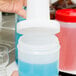 A hand pouring blue liquid from a plastic container with a white spout and cap.