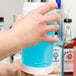 A person holding a Carlisle white container with blue liquid.