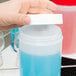 A person pouring blue liquid from a white Carlisle plastic container with a white cap.