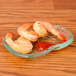 A 10 Strawberry Street ocean clear glass elliptical dish with shrimp and sauce on a wood table.