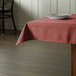 A square mauve tablecloth on a table with plates on it.