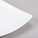 A white 10 Strawberry Street Aurora square porcelain plate with a curved edge on a gray surface.