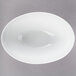 A white oval porcelain bowl with a small rim on a gray surface.