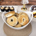 A white porcelain bowl with cut outs holding bagels on a table.