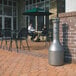 A Rubbermaid traditional free standing cigarette receptacle on a brick patio table with a green umbrella.