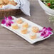 A white rectangular porcelain handled platter with pastries on a table.