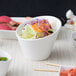 A close up of a bowl of salad with vegetables in a white 10 Strawberry Street Whittier tall slant bowl.