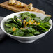 A white porcelain ribbed footed bowl filled with spinach salad on a table.
