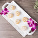 A white 10 Strawberry Street rectangular porcelain tray with handles on a table with donuts and flowers.