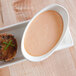 A 10 Strawberry Street Whittier white porcelain oval bowl with crab cake and sauce on a table.