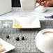 A person using a white Whittier square porcelain tid bit tray to pour coffee into a white cup on a table with food.