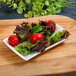 A white rectangular porcelain 10 Strawberry Street tid bit tray with a plate of salad on a wood surface.