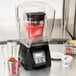 A Waring commercial blender with a container of strawberries on the counter.