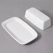 A white rectangular porcelain butter dish with a lid on a gray surface.