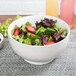 A white 10 Strawberry Street Whittier footed bowl filled with salad with strawberries and blueberries.