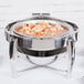 A Vollrath stainless steel round chafing dish with food inside.